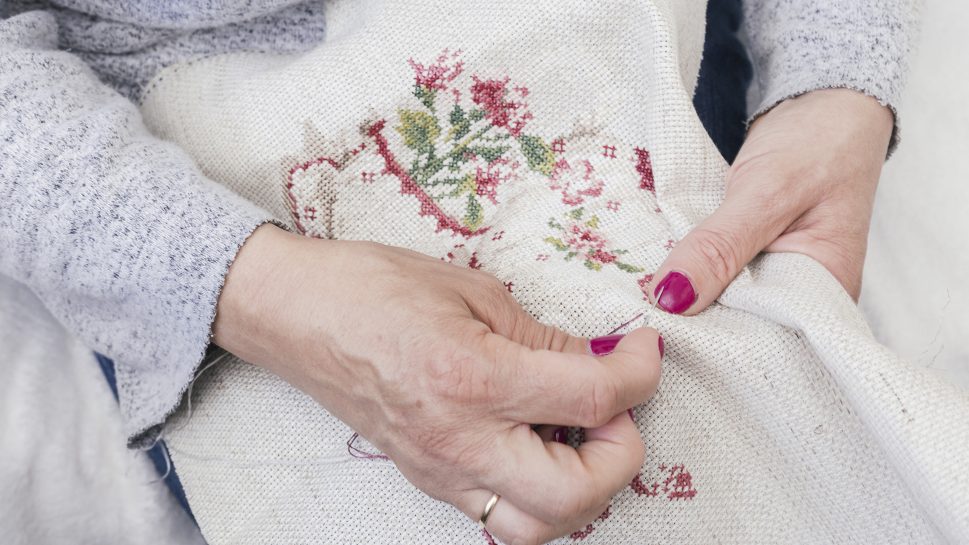 a lady with painted fingernails cross stitching
